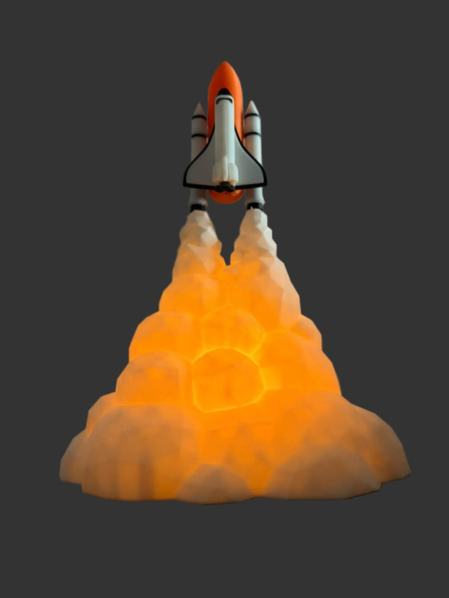 A space shuttle model launching from an illuminated glowing cloud base, set against a plain gray wall and dark wooden surface.