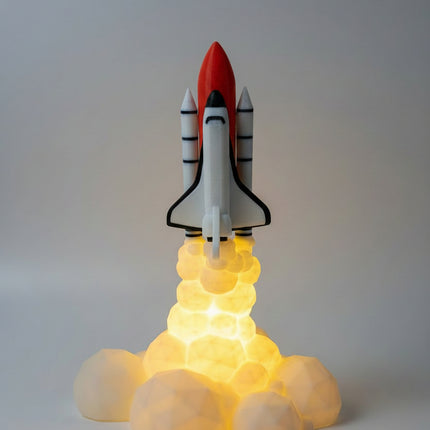 A small space shuttle model displayed on a glowing yellow base that simulates exhaust, set against a dimly lit wall and wooden surface.